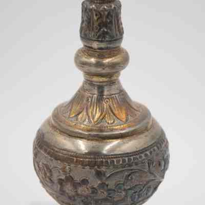 Body of rose water sprinkler from the coffee service given to the Jordans by Sheikh Ahmad Al-Jaber Al-Sabah.: Up close image of the body of the silver rose water sprinkler decorated with debossed flowers, leaves, and vines. The gold detail on the leaves is faded.
