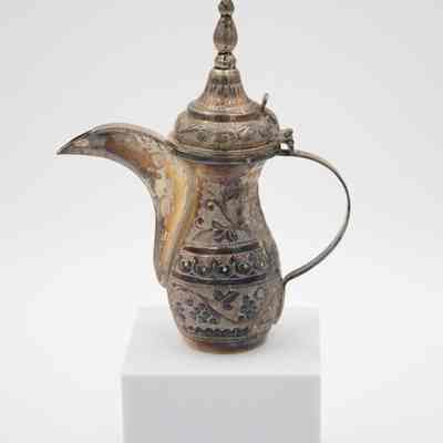 The smaller coffee pot from the coffee service given to the Jordans by Sheikh Ahmad Al-Jaber Al-Sabah.: Image of the silver debossed coffee pot decorated with vines and a pointed lid.