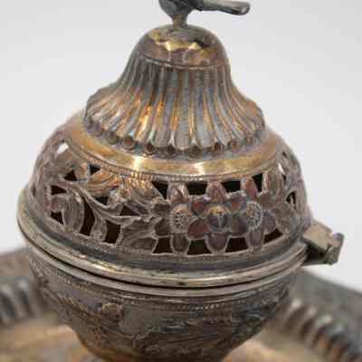 Body of the incense burner given to the Jordans by Sheikh Ahmad Al-Jaber Al-Sabah.: Up close image of the body of the silver globe-shaped incense burner on circular footed tray. They are both decorated with debossed flowers and vines. There is a small cast bird on the top of the incense burner, it is likely a falcon.