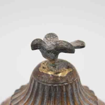 Cast bird on top of the incense burner given to the Jordans by Sheikh Ahmad Al-Jaber Al-Sabah.: Up close image of the top lid of the silver incense burner. There is a small cast bird, likely a falcon, with debossed wings on the top.