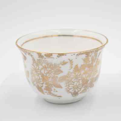 Small cup from the coffee service given to the Jordans by Sheikh Ahmad Al-Jaber Al-Sabah.: Up close image of the small bone China handle-less teacup decorated with gold foil flowers and leaves. There is a thin gold foil line on the inside rim.