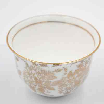 Small cup from the coffee service given to the Jordans by Sheikh Ahmad Al-Jaber Al-Sabah.: Up close image of the small bone China handle-less teacup decorated with gold foil flowers and leaves. There is a thin gold foil line on the inside rim.