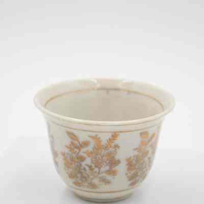 Small cup from the coffee service given to the Jordans by Sheikh Ahmad Al-Jaber Al-Sabah.: Up close image of the small bone China handle-less teacup decorated with gold foil flowers and leaves. There is a thin gold foil line on the inside rim.