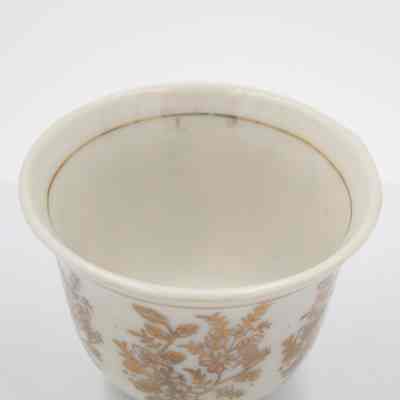 Small cup from the coffee service given to the Jordans by Sheikh Ahmad Al-Jaber Al-Sabah.: Up close image of the small bone China handle-less teacup decorated with gold foil flowers and leaves. There is a thin gold foil line on the inside rim.
