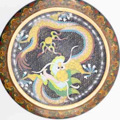 Black enamel bowl with gold dragon on wood stand: A closer and brighter birds-eye view of the bowl. The top edge and the center inside is visible. The top edge is decorated with swirls. Inside, a golden dragon with big eyes and an open mouth lies.