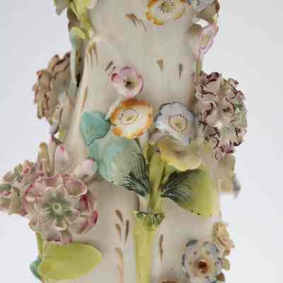 Details on the porcelain bud vases.: Up close image of one of the two porcelain vases decorated with pastel hand-painted encrusted flowers. The flowers are pink, blue, purple, red, and orange with green leaves. There is also gold foil detail around the edges of the vase and throughout the piece.