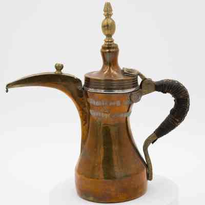 Brass and copper coffee pot: A copper coffee pot with leather-wrapped handle, brass details, and stamped Arabic script.