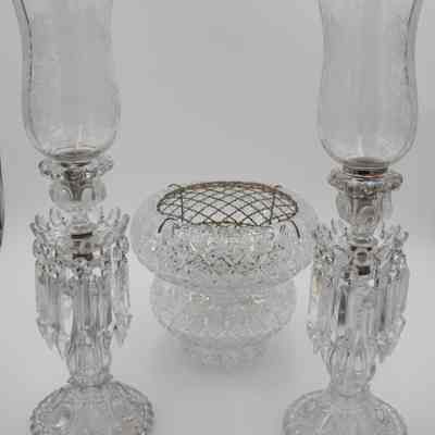 Flower frog and candelabras: The image showcases an arrangement featuring a crystal cut vase with a mesh metal flower frog centerpiece with two candelabras, each adorned with hurricane shades and dangling prisms.