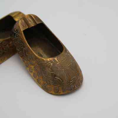 Brass shoe ashtray: The image displays brass shoe-shaped ashtrays adorned with intricate engraved flower designs on their surfaces.