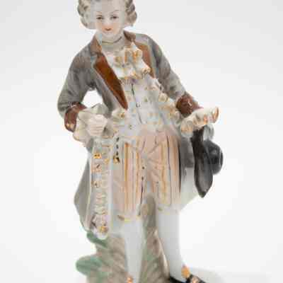 Hand-painted porcelain figurine of a man holding a black hat from Japan.: Up close image of painted porcelain figurine of a man dressed in regency-wear and holding a black hat.
