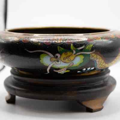 Black enamel bowl with gold dragon on wood stand: The outside of the bowl features the face of a second golden yellow dragon. The wooden stand is dark, with 3 feet elevating it.
