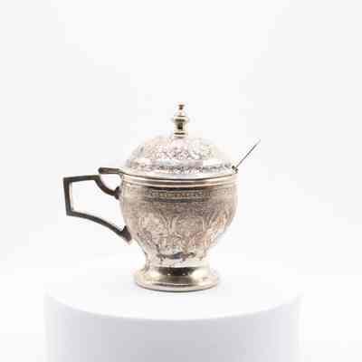 Persian silver engraved sugar bowl with lid and spoon.: Image of the silver engraved sugar bowl with the lid closed and spoon sitting in it. Both pieces are engraved with Persian designs.