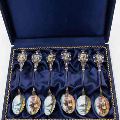 Set of six silver spoons decorated with scenes of Kuwait in a blue case.: Image of the set of six silver spoons in a blue felt case. There are two different designs enameled on both the handle and bowl. One spoon has a camel and Bedouin on the handle with a scene of an oil rig system on the bowl. The handle is also decorated with small silver details and there is a knight helmet on the end. The other design has an oil ship on the handle with camel and Bedouin man in the desert on the bowl.