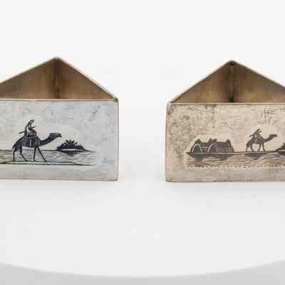 Napkin rings: A pair of triangular metal napkin holders features Kuwaiti oasis scenes engraved on them.