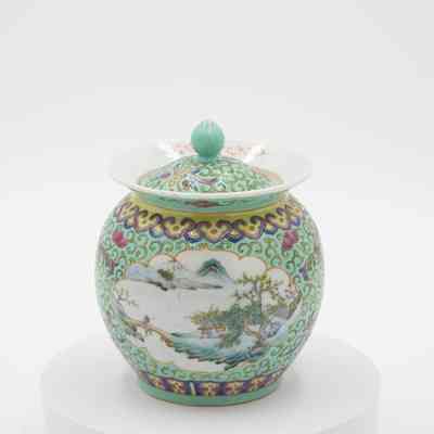 Porcelain jar with mint green Hong Kong scene.: Image of the mint green jar with yellow swirls. It is also decorated with a painted scene of a house, man, and bridge in the mountains.