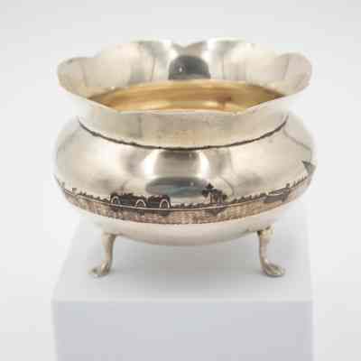 Footed bowl: A polished silver footed bowl with a scalloped rim features an etched oasis scene, complete with palm trees and distant structures.