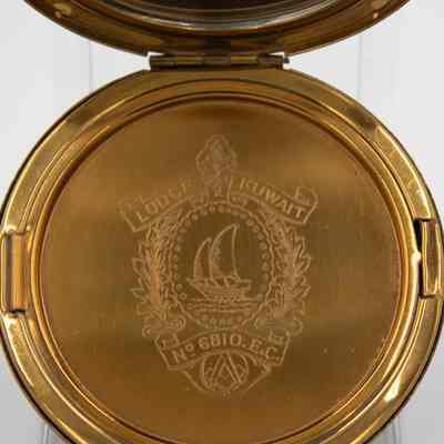 Engraving of the Kuwait Masonic Lodge 6810 seal on the inside of the circular gold compact given to Mrs. Jessie Jordan at a Ladies' Night in 1952.: Up close image of the engraved seal of Kuwait Masonic Lodge 6810 on the inside of the compact. The seal reads" LODGE KUWAIT No. 6810. E.C." and there is a Kuwaiti two-masted dhow in the center. It is surrounded by two branches and there is the infamous Masonic compass at the bottom.