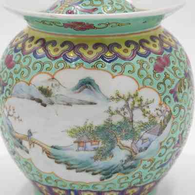 Scene on the porcelain mint green jar.: Up close image of the mint green jar with yellow swirls. It is also decorated with a painted scene of a house, man, and bridge in the mountains.