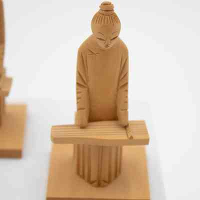 One of the carved wooden figurines of men playing instruments.: Up close image of one of two carved wooden figurines of men playing the Chinese zither. They are carved from light brown cedar wood.