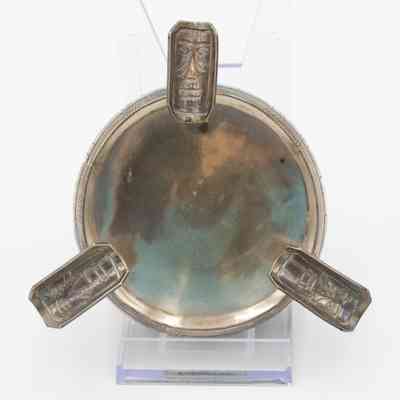 Tiki ashtray: The image shows a small silver ashtray with engraved tiki-style cigarette holders elegantly crafted.