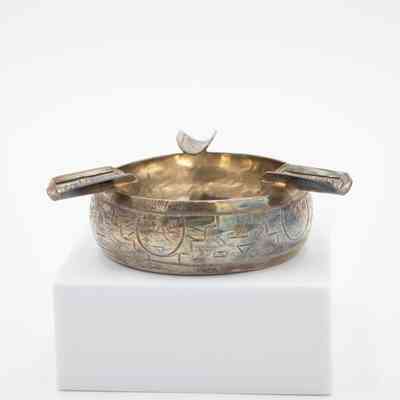 Tiki ashtray: A silver ashtray with engraved tiki designs has three unique cigarette holders above.