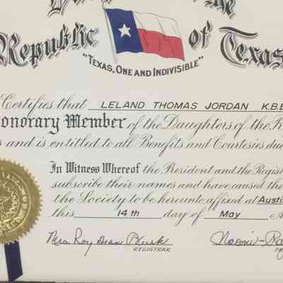 Daughters of the Republic of Texas Honorary Member Certificate: Close-up image of the certificate in its glass case. The registrar and president have both signed their names in their sections. The seal of the Daughters of the Republic of Texas is gold and features the state star in their seal.