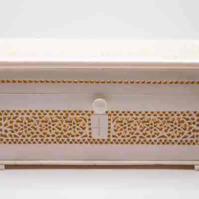 Carved rectangular ivory box from India.: Up close image of the ivory carved rectangular box with a hinged lid and push button on the front. The box has cutout designs on all sides.