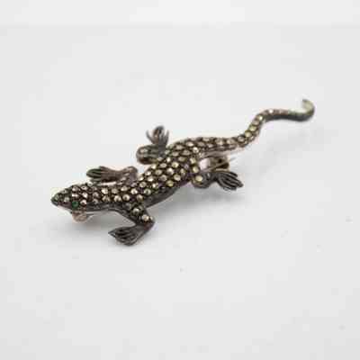Small lizard brooch that belonged to Mrs. Jessie Jordan.: Up close image of the small lizard-shaped brooch, it is made of silver embedded with diamonds and two emerald eyes. It is roughly two inches in length.