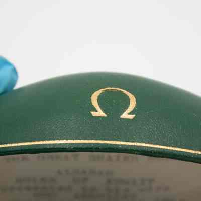 Green Omega case that holds the bracelet that was given to Mrs. Jessie Jordan by Umm Abdullah Mubarak.: Up close image of the gold Omega logo on the lid of the green case.