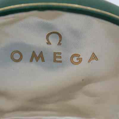 Green Omega case that holds the bracelet that was given to Mrs. Jessie Jordan by Umm Abdullah Mubarak.: Up close image of the inside lid of the green Omega case. It is white satin with "OMEGA" and logo printed in gold.