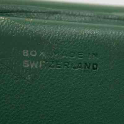 Bottom of the green Omega case that holds the bracelet that was given to Mrs. Jessie Jordan by Umm Abdullah Mubarak.: Up close image of the bottom of the green Omega watch case. It is embossed with "BOX MADE IN SWITZERLAND."