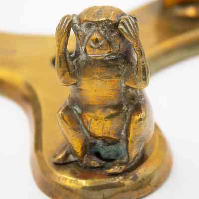 Image of "hear no evil" monkey: Close up image of the "hear no evil" monkey. The brass monkey is holding its hands over its ears, representing Kikazaru from the original maxim.