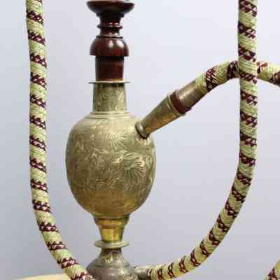 Base of bubble pipe: The ornate hookah features intricate metalwork and a colorful, woven hose, positioned on a wooden surface