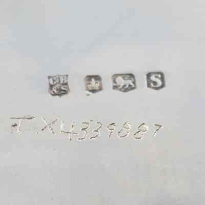 Silversmith marks and Jordan inventory number on the back of the silver plate from Kuwait Masonic Lodge 6810.: Up close image of the stamped silversmith marks on the back of the plate. The first mark is a "C, B & S," denoting the company. The second is a small crown, denoting that English city of origin, which in this case is Sheffied. The third is a small lion, which is the passant lion indicating the piece is genuine silver. The fourth and final is a "S," which indicates the year it was made (1961). The etched in number under the marks is believed to have been done by the Jordans and reads "TX4339887."
