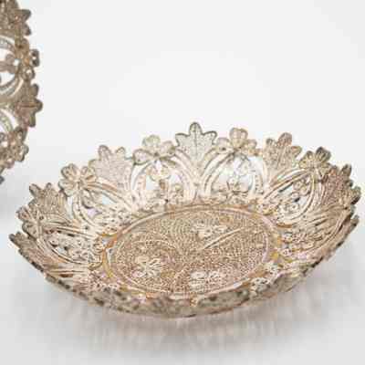Small round silver filigree lace tray.: Image of the round silver filigree lace tray laying flat. There is a leaf and floral design around the edge and a three-stemmed plant in the center.