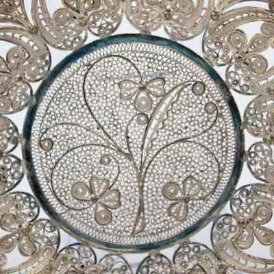 Center of the round silver filigree lace tray.: Up close image of the center of the round silver filigree lace tray. There is a three-stemmed plant and clover design in the middle.