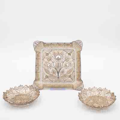 One square filigree lace tray and two circular filigree lace trays.: Image of the set of three filigree lace trays. The square tray is propped up in the back center. There are two circular trays on either side.