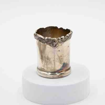 Silver Cup: Image of the silver cup. The mouth of the cup is irregular with a scroll finish. There is tarnish on the lower half of the cup.