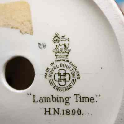Bottom of the figure.: The bottom of the figure shows the company’s name, logo, and the figures name. “Made in England, Royal Doulton England. “Lambing Time” H.N. 1890.” The companies logo is a lion with a crown, standing on top of a crown.