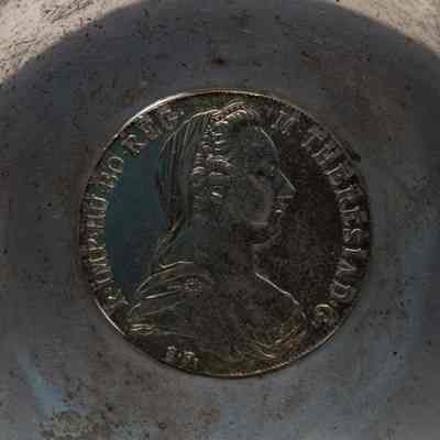 Maria Theresa Coin Obverse: Close-up image of the silver coin featuring a bust of Austrian Empress Maria Theresa facing to the left. Surrounding the bust is the Latin inscription "M. THERESIA D. G. R. IMP. HU. BO. REG." This roughly translates to "Maria Theresa, by the grace of God, Empress of the Romans, Queen of Hungary and Bohemia."
