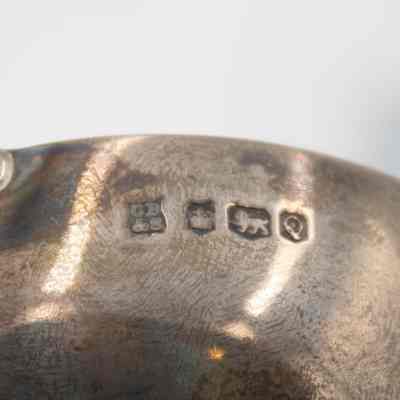 Silversmith marks found on the side of the silver trophy cup presented to the Jordans by the Caledonian Society.: Up close image of the silversmith marks on the side of silver trophy cups. From left to right, the stamp "CB&S" indicated the maker, the crown indicates it was made in Sheffield, the passant lion indicates the piece is genuine silver, and the "Q" indicates the year it was produced.