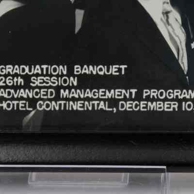 Photograph Caption: Close-up image of the caption found in the bottom middle of the photograph. In capital white letters it reads "Graduation Banquet 26th Session Advanced Management Program Hotel Continental, December 10, 1954."