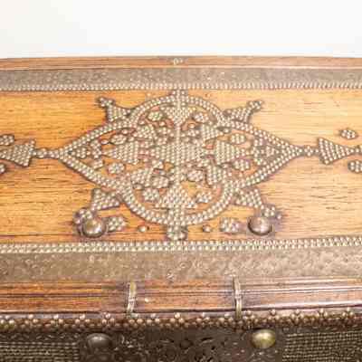 Top of wedding chest: The image shows a detailed teakwood chest adorned with intricate brass designs, once used for trade.