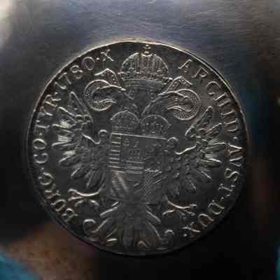 Maria Theresa Coin Reverse: Close-up image of the bottom of the coin dish's bowl which features the coin's reverse. On the reverse is the coat of arms of Maria Theresa, as well as the Latin inscription "ARCHID. AVST. DUX BURG. CO. TYR. 1780 X" which can roughly translate to "Archduchess of Austria, Duchess of Burgundy, Countess of Tyrol. 1780." The X is a Christian cross.