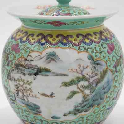 Scene on the porcelain mint green jar.: Up close image of the mint green jar with yellow swirls. It is also decorated with a painted scene of a man on a boat in the water and a house.