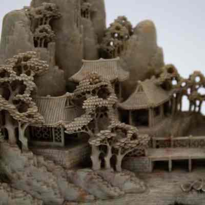 Grey stone-carved Shoushan village.: Up close image of part of one of the grey-green stone carved villages on dark brown stands. The villages are Shoushan-style with trees, people, and Chinese houses.