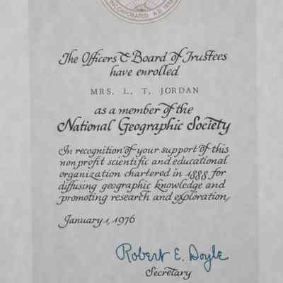 Certificate Close-up: Close-up image of the certificate for the Geographic Society. The National Geographic Society's logo of a circular map projection of the Americas in brown ink is featured at the top of the enrollment certificate. The box in which the text is contained in is a mint green while the surrounding area is an off white. The certificate itself reads, "The Officers & Board of Trustees have enrolled Mrs. L.T. Jordan as a member of the National geographic Society In recognition of your support of this non profit scientific and educational organization chartered in 1888 for diffusing geographic knowledge and promoting research and exploration." The secretary Robert E. Doyle has signed his name in a blue ink.