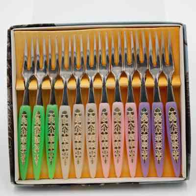 Japanese "Little Fork" set.: Up close image of the set of 12 little forks with purple, pink, white, and green handles and silver prongs. They sit in their original box with a yellow backing.