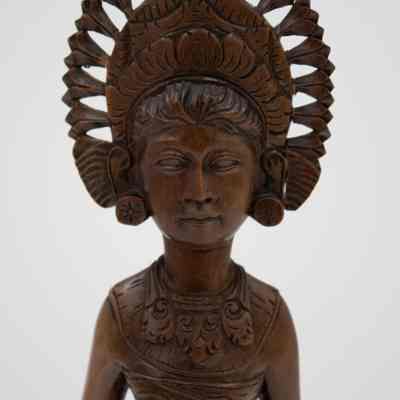 Carved bust of the wooden tall woman in Balinese ceremonial dress.: Up close image of the carved wooden tall woman dressed in a traditional Balinese dress. She is wearing a large necklace and bun udeng tiara.