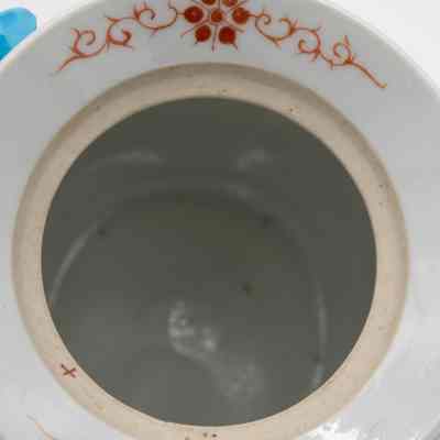 Inside of the mint green porcelain jar.: Up close image of the top and inside of the porcelain jar. The top rim in white with red swirls and a flower design.